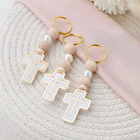 Decorative keychain with cross designs and pearl-like beads on a textured surface.