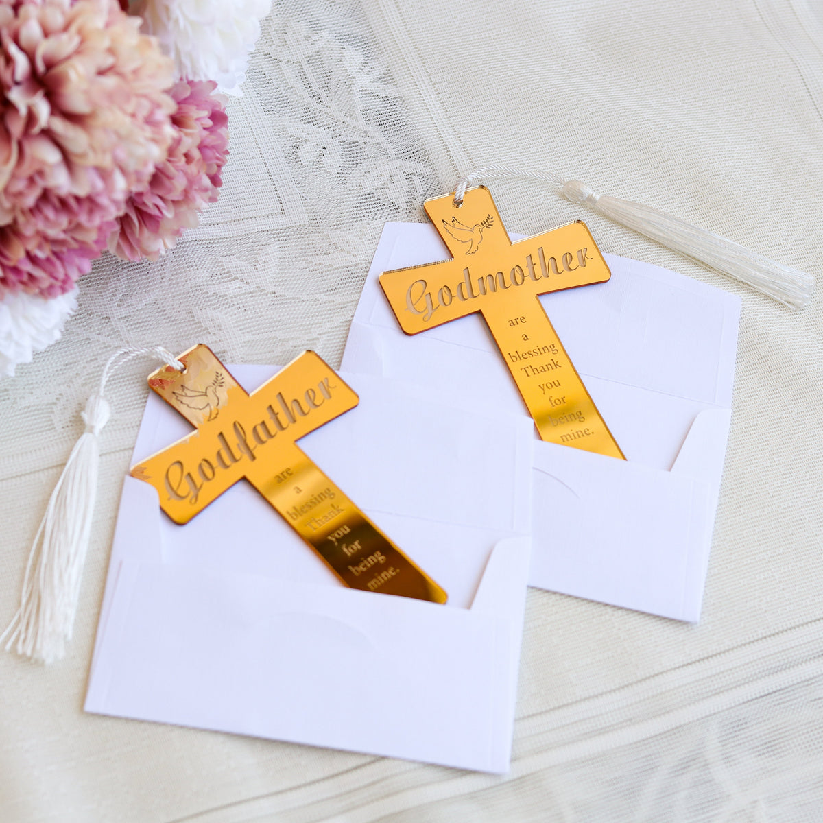 Gold 'Godfather' cross cards on white paper with tassels and flowers in the background.