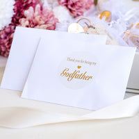 Card with 'Thank you for being my Godfather' text on a white surface with flowers in the background