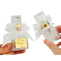 Two glass bottles labeled 'Holy Water' with decorative ribbons and crosses, held by hands against a white background.