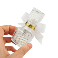 Clear glass bottle with gold cap and white bow held by a hand on a white background