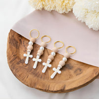 Set of first communion favors with cross designs on a wooden surface with flowers in the background.