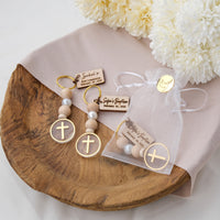 You will love these personalized baptism keychain cross favors. These keychains are crafted with natural wood and pearl beads, and they feature a design with a cross at the end. also customize them with a tag that has the name and date of the baptism