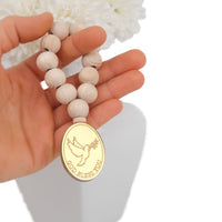 Hand holding a mini rosary with wooden beads and a gold medallion featuring a dove and 'God Bless You' text.