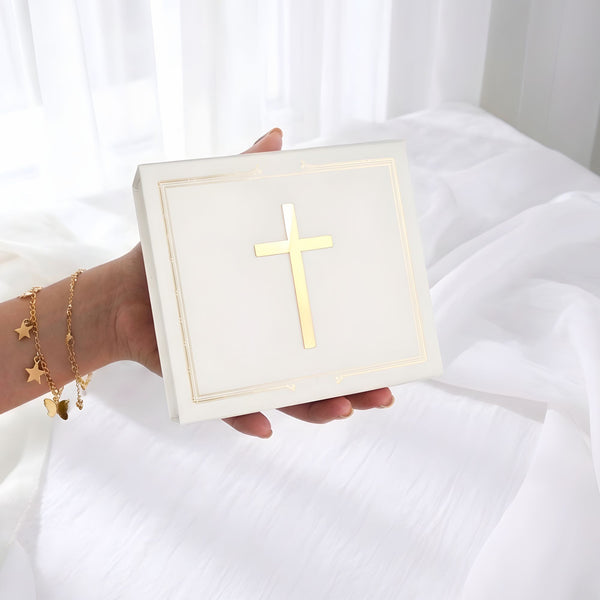 Hand holding a white box with a gold cross design on a white background