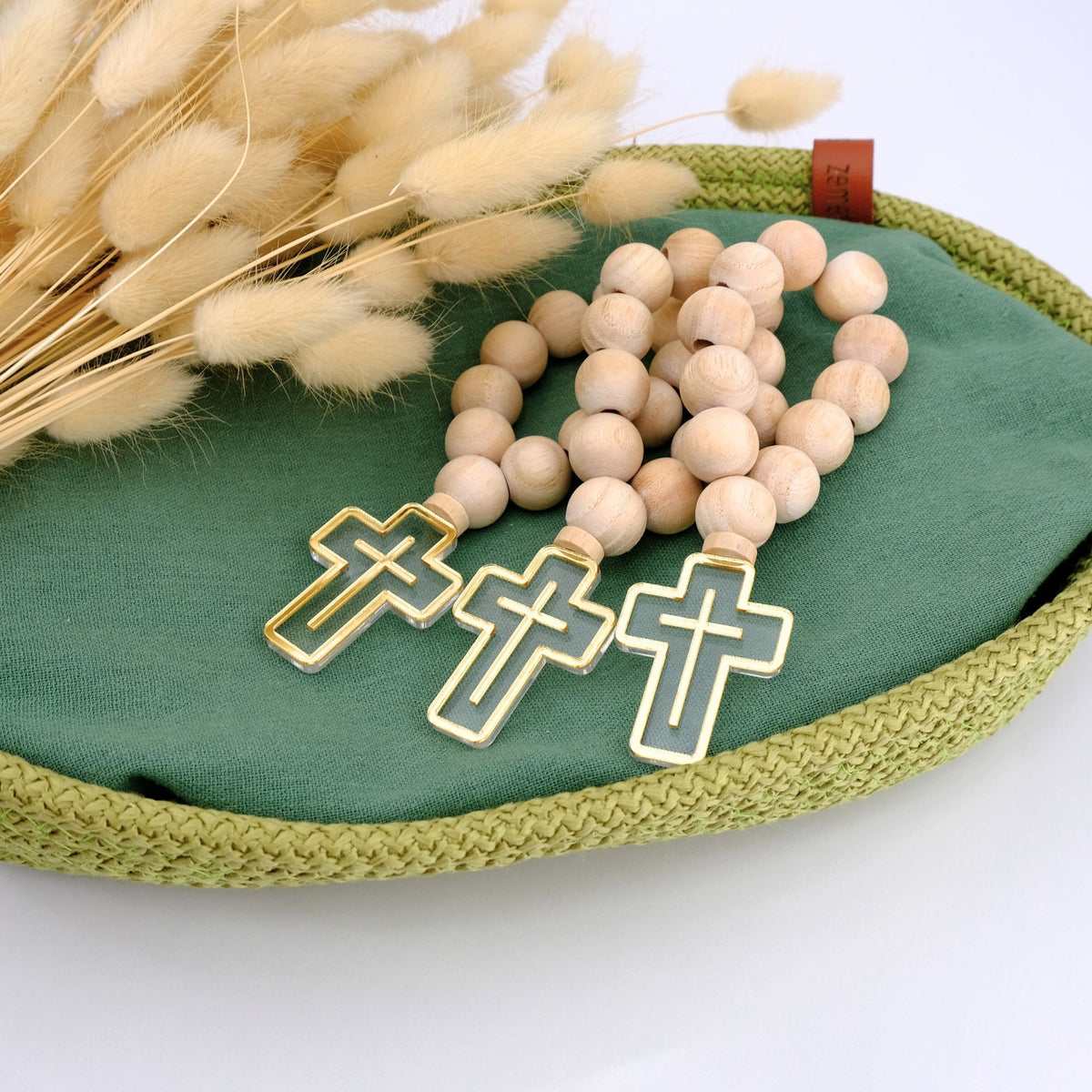 Wooden rosary with gold cross charms on a green fabric surface with dried flowers.