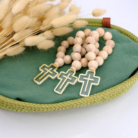 Wooden rosary with gold cross charms on a green fabric surface with dried flowers.