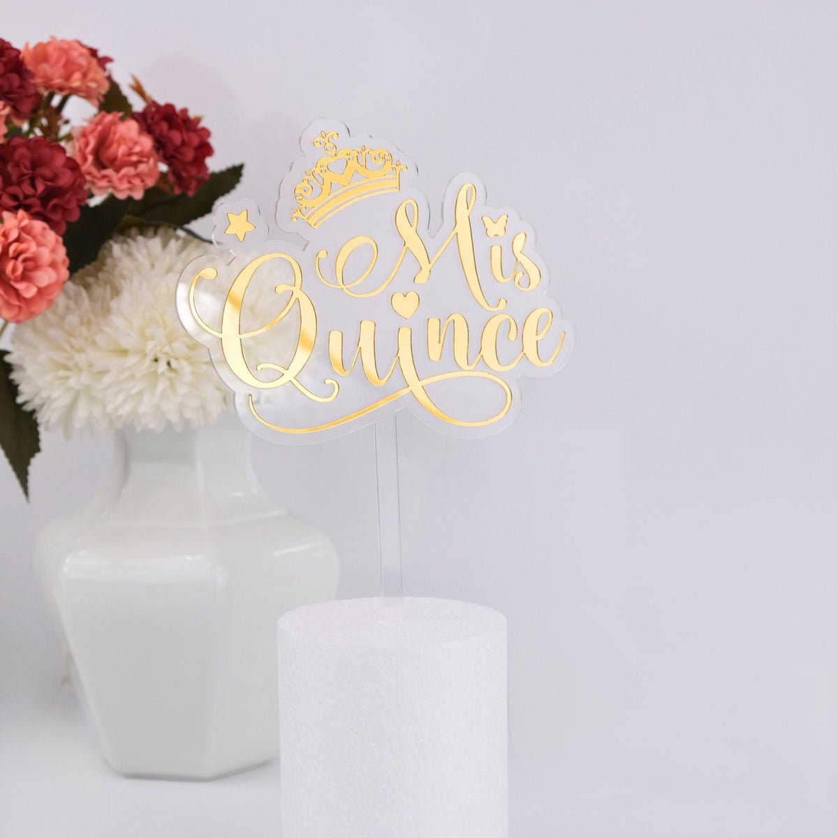 Decorative cake topper with 'Mis Quince' text and flowers in the background