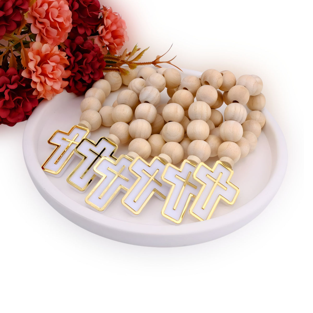 Wooden beaded mini rosary guest favors with gold and white pendants on a white plate with flowers in the background