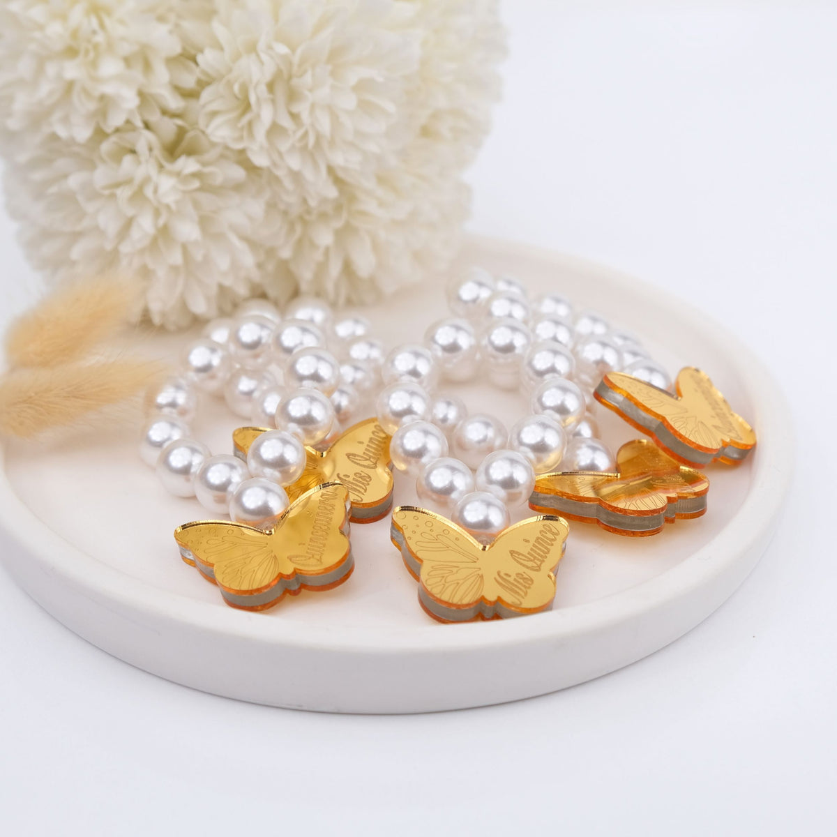 Gold butterfly-shaped pendants on a pearl mini rosaries with a white decorative item in the background.