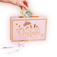 Pink gift bag with 'Mis Quince' text, money being inserted, on a white background
