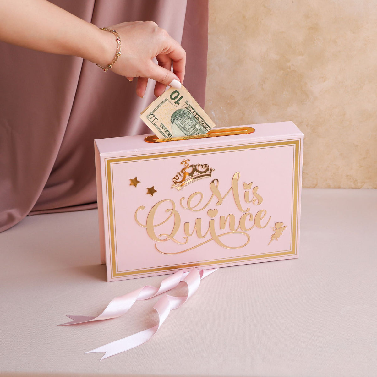 Pink 'Mis Quince' box with a hand inserting money, on a beige background