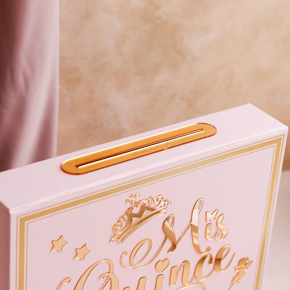 Pink box with gold text and design on a beige background