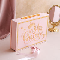 Pink gift box with 'Mis Quince' text on a decorative surface with a mirror.