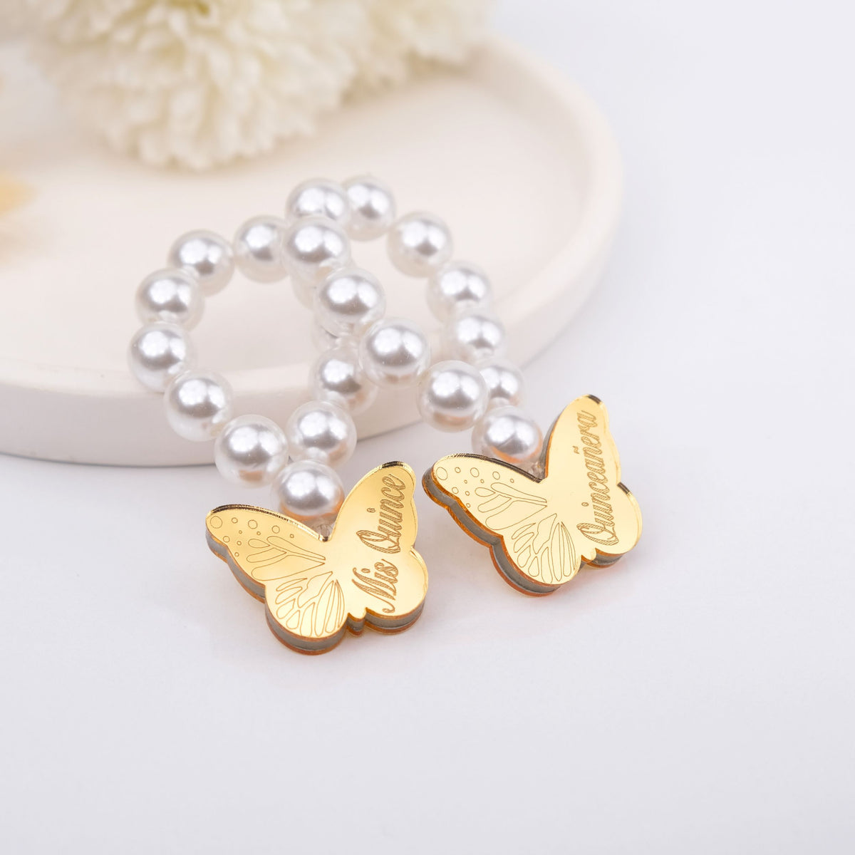 Gold butterfly charms on a pearl bracelet mini rosaries with 'Quinceanera' engraving on a light background