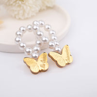 Gold butterfly charms on a pearl bracelet mini rosaries with 'Quinceanera' engraving on a light background