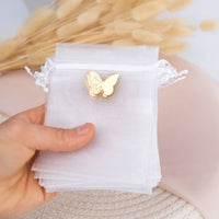 Gold butterfly charm on a white favor pouch held by a hand with a light background