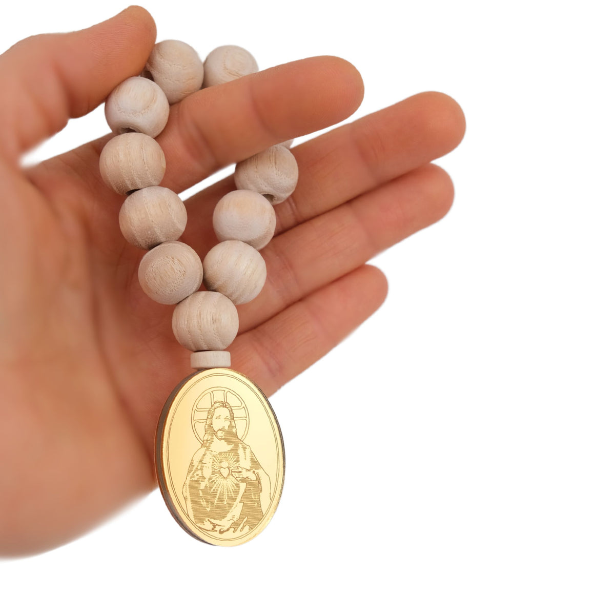 Hand holding a rosary with a gold medal featuring an image of a Jesus Christ figure on a white background